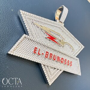 Puede incluir: Un colgante de plata con un dise&ntilde;o en forma de estrella, cubierto de piedras de circonita c&uacute;bica transparentes. El colgante presenta un rayo rojo y el texto "EL-BRUNOSSS" en rojo.