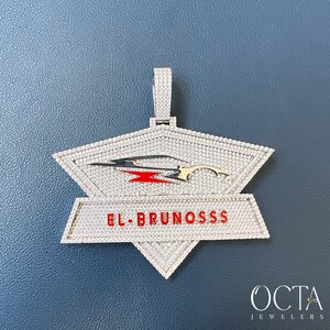 Puede incluir: Un colgante de plata con un dise&ntilde;o incrustado de diamantes que presenta un coche estilizado y el texto "EL BRUNOSSS".