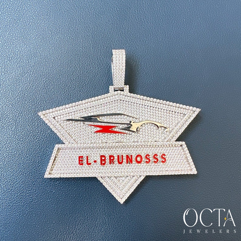 Puede incluir: Un colgante de plata con un dise&ntilde;o incrustado de diamantes que presenta un coche estilizado y el texto "EL BRUNOSSS".