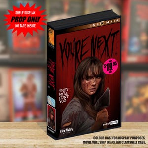 Puede incluir: Una caja rectangular estilo VHS para la película You're Next. La portada presenta un fondo rojo oscuro con el título en negro, una ilustración central de una persona con la cara ensangrentada sosteniendo una hoja, y el texto They Will Hunt You.