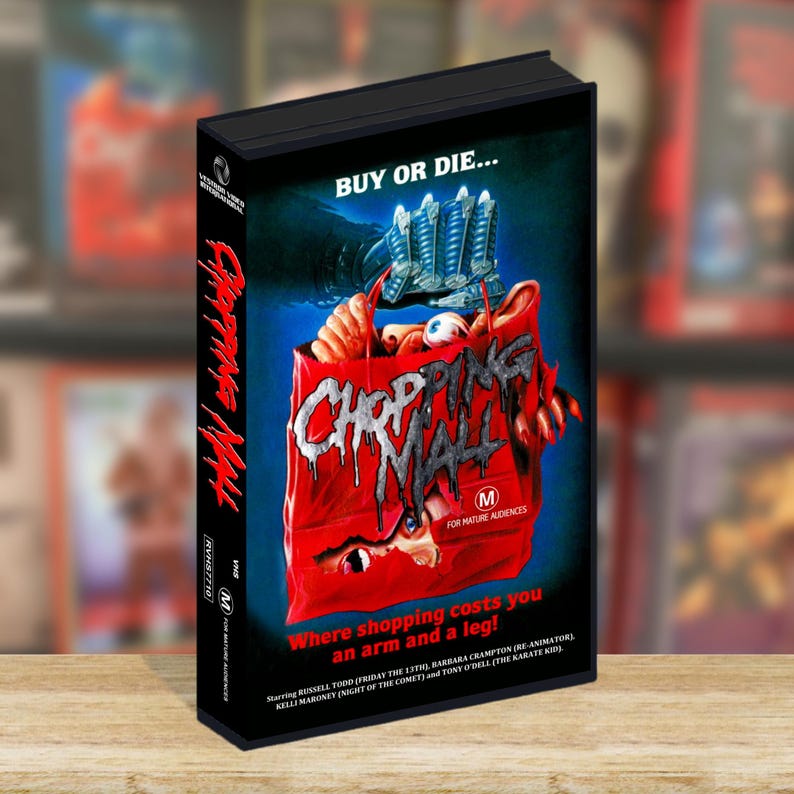 May include: A VHS tape of the film Chopping Mall with a black case. The cover art features a red shopping bag with a robotic hand, a human eye, and the text Buy or Die and Where shopping costs you an arm and a leg. The spine shows the title in red.
