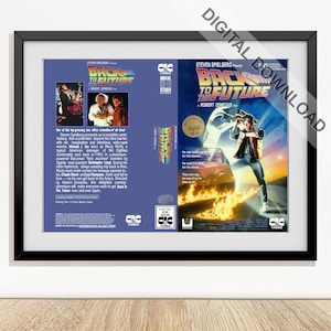 Könnte beinhalten: Ein gerahmter Druck des VHS-Covers des Films "Zurück in die Zukunft". Das Kunstwerk zeigt den Filmtitel und eine Szene mit einem Auto und einer Figur. Das VHS-Gehäuse ist blau und trägt den Text "Digital HiFi Stereo".