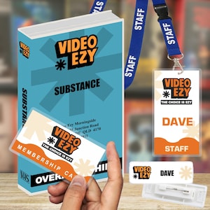 以下が含まれることがあります： Video EzyのVHSケース「Substance」、会員カード、Daveと書かれたスタッフ用ネックストラップ付きバッジ、長方形の名札。各アイテムには、オレンジと黒のVideo Ezyロゴと白い文字が、水色または白の背景にデザインされています。