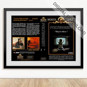 May include: A framed print of the VHS cover for the movie "Poltergeist." The cover features the movie title and the tagline "They're Here." A young girl is in front of a television screen. The frame is black.