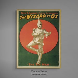 May include: A vintage poster advertising a musical extravaganza of "The Wizard of Oz" featuring the Tin Man in a red circle against a green background. The poster has gold trim and the text "FRED R. HAMLIN'S MUSICAL EXTRAVAGANZA" at the top.