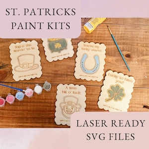 May include: St. Patrick's Day paint kits with various designs, including a leprechaun, horseshoe, and four-leaf clover. The kits include wooden cutouts, paint, and brushes. The text on the image says "St. Patrick's Paint Kits" and "Laser Ready SVG Files."