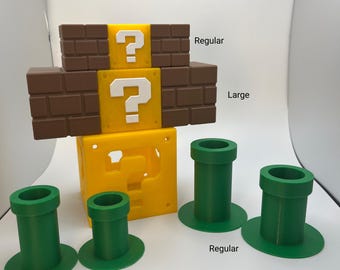 May include: A collection of 3D-printed items inspired by a video game. Includes a yellow question mark block, brown brick blocks, and green pipes in various sizes. The text "Regular", "Large", and "Small" are visible.
