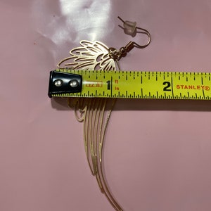 Puede incluir: Pendiente de metal dorado con dise&ntilde;o de ala. El pendiente mide aproximadamente 2,5 cm de largo.