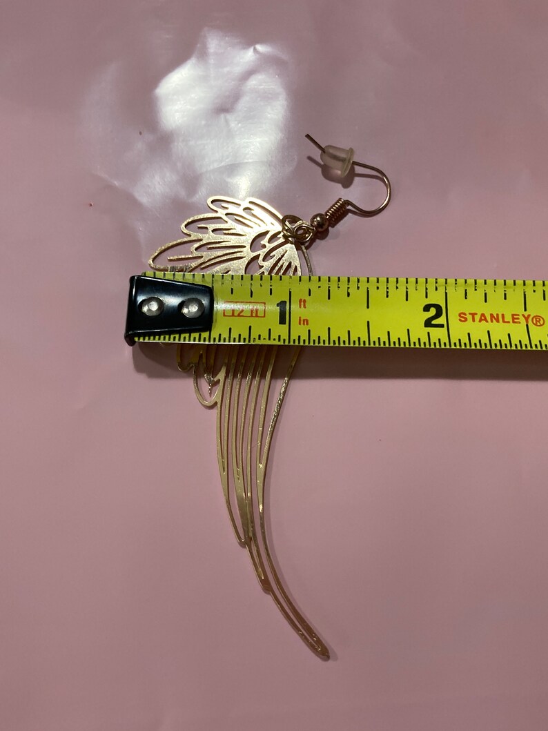 Puede incluir: Pendiente de metal dorado con dise&ntilde;o de ala. El pendiente mide aproximadamente 2,5 cm de largo.