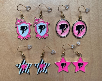 Pendientes rosas con estrellas y estrellas redondas ovaladas con rayas negras y bañados en oro blanco