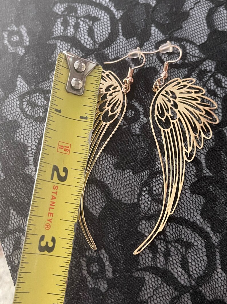 Puede incluir: Pendientes de alas de &aacute;ngel de tono dorado con cierre de gancho. Los pendientes miden aproximadamente 5 cm de largo.