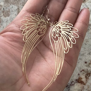 Puede incluir: Un par de pendientes colgantes de tono dorado con un delicado dise&ntilde;o calado de alas de &aacute;ngel.