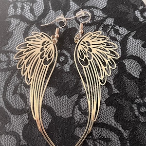 Puede incluir: Pendientes colgantes de color dorado con un dise&ntilde;o delicado e intrincado que se asemeja a alas de &aacute;ngel.