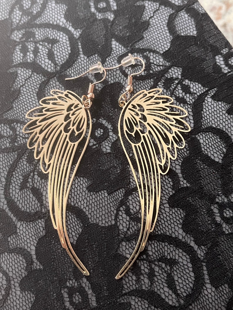 Puede incluir: Pendientes colgantes de color dorado con un dise&ntilde;o delicado e intrincado que se asemeja a alas de &aacute;ngel.