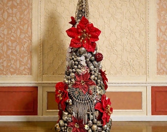 May include: A decorative Christmas tree made of silver-toned ornaments and red poinsettias. The tree is cone-shaped and adorned with various metallic embellishments, including beads and decorative elements. The tree is set against a backdrop of a wall with decorative panels.