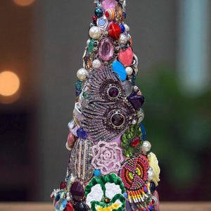 May include: A decorative Christmas tree sculpture adorned with a variety of colorful beads, pearls, and gemstones. The tree features a cone shape and is embellished with a mix of textures and sizes, creating a unique and festive design.