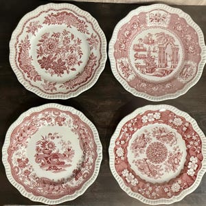 Może przedstawiać: Cztery biało-czerwone talerze dekoracyjne z falistymi krawędziami. Każdy talerz ma inny kwiatowy lub krajobrazowy wzór w kolorze czerwonym. Talerze są ułożone w kwadrat, prezentując różnorodność wzorów.