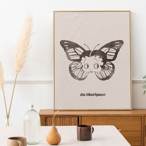 May include: A black and white illustration of a butterfly with a cartoon face. The butterfly is on a beige background with the text "La Mariposa" printed below it.
