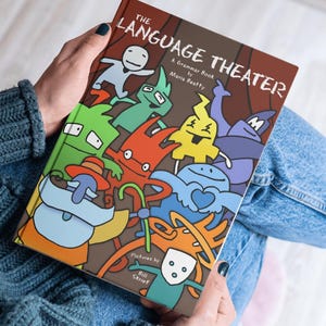 Adult holding The Language Theater visual grammar book, highlighting its educational illustrated design.