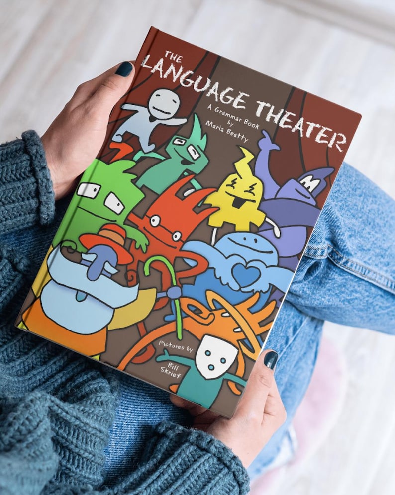 Adult holding The Language Theater visual grammar book, highlighting its educational illustrated design.
