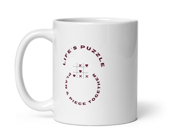 May include: White ceramic mug with a maroon circle design that reads "Life's Puzzle Piece & Plan Together" with a tic-tac-toe board inside the circle.