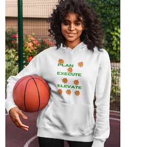 May include: White hoodie with a green and orange graphic design featuring the words "PLAN EXECUTE ELEVATE" and several cartoon pumpkins. The person is holding a basketball.