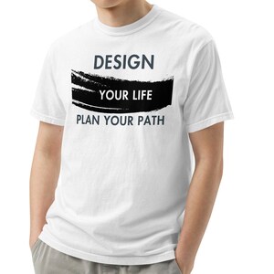 Pode incluir: Camiseta branca com um design de pinceladas pretas e o texto "DESIGN YOUR LIFE PLAN YOUR PATH" em cinza.