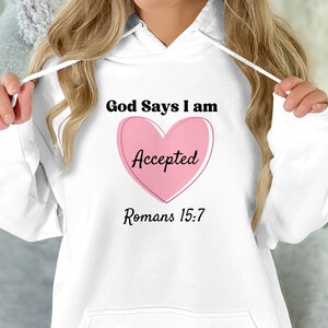 Pode incluir: Moletom branco com capuz com um coração rosa e o texto "God Says I am Accepted Romans 15:7"