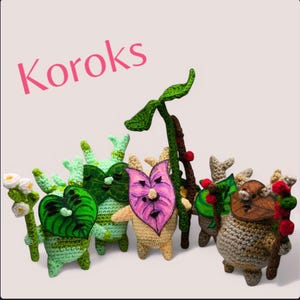 Könnte beinhalten: Fünf gehäkelte Korok-Plüschtiere aus dem Videospiel The Legend of Zelda: Breath of the Wild. Die Plüschtiere sind grün, braun, beige und rosa mit verschiedenen Blattdesigns. Das Wort "Korok" ist in rosa Buchstaben oben im Bild geschrieben.