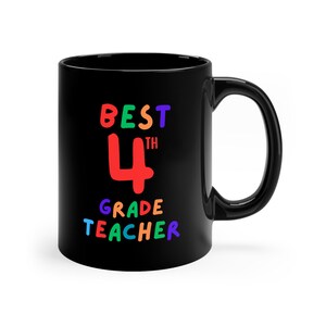 Puede incluir: Taza de café negra con el texto "BEST 4TH GRADE TEACHER" en colores arcoíris.