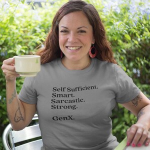 Op de afbeelding: Een grijs T-shirt met de tekst "Self Sufficient. Smart. Sarcastic. Strong. GenX." gedrukt op de voorkant.