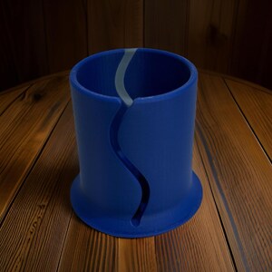 Op de afbeelding: Een cilindrische blauwe houder met een doorlopende, verticale, S-vormige uitsparing aan de zijkant. Het object heeft een uitlopende voet en een gladde, matte afwerking, met een lichtgrijze binnenvoering zichtbaar door de opening in de voorwand.