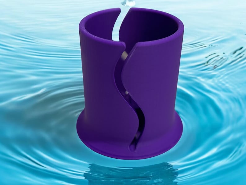 Op de afbeelding: Een paarse cilindrische houder met een verticale, S-vormige golvende gleuf aan de zijkant. Het object heeft een uitlopende basis en een gladde, matte afwerking, rechtop geplaatst in een blauw wateroppervlak met rimpelingen vanuit het midden.