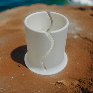 Op de afbeelding: Een witte keramische garenkom met een gladde, matte afwerking en een brede, ronde basis. De kom heeft een enkele, doorlopende verticale opening die van de bovenrand naar de basis buigt, ontworpen voor het vasthouden en afgeven van garen.