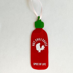 May include: Red and green hot chili sauce bottle ornament with a white rooster and the text "Hot Chili Sauce Spice of Life".