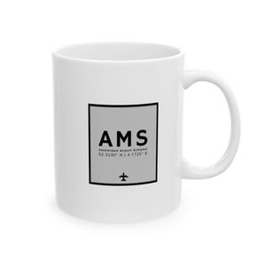 Op de afbeelding: Witte keramische mok met een zwart en grijs ontwerp. Het ontwerp bevat de tekst "AMS Amsterdam Airport Schiphol 52.3130° N | 4.7725° E" en een klein vliegtuigsymbool.
