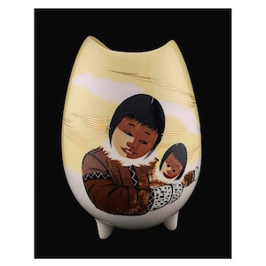 May include: A ceramic vase with a yellow glaze and a painted design of two Indigenous people. The vase has a rounded shape with three small feet.
