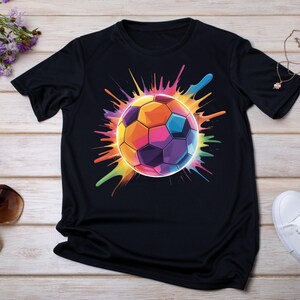 May include: Black t-shirt featuring a vibrant, colorful soccer ball design. The soccer ball is rendered in a spectrum of hues, including orange, yellow, blue, and purple, with a splash effect radiating outwards. The shirt is made of a soft material.