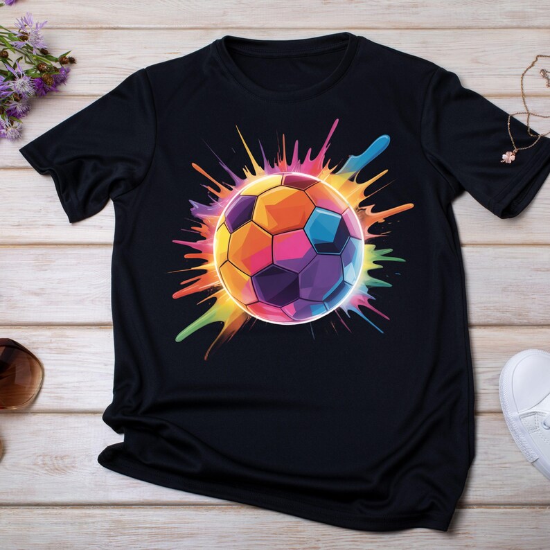 May include: Black t-shirt featuring a vibrant, colorful soccer ball design. The soccer ball is rendered in a spectrum of hues, including orange, yellow, blue, and purple, with a splash effect radiating outwards. The shirt is made of a soft material.