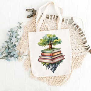 Puede incluir: Un bolso tote de color crema con una ilustraci&oacute;n en acuarela de un &aacute;rbol que crece de una pila de libros. El &aacute;rbol tiene hojas verdes y un tronco marr&oacute;n. Los libros son en tonos de rojo, naranja y verde. El bolso tiene asas color crema.