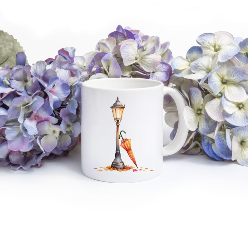 Pode incluir: Caneca de cer&acirc;mica branca com uma ilustra&ccedil;&atilde;o em aquarela de um lampi&atilde;o vintage, um guarda-chuva laranja e folhas de outono. A caneca &eacute; cercada por flores de hort&ecirc;nsia roxas e azuis.