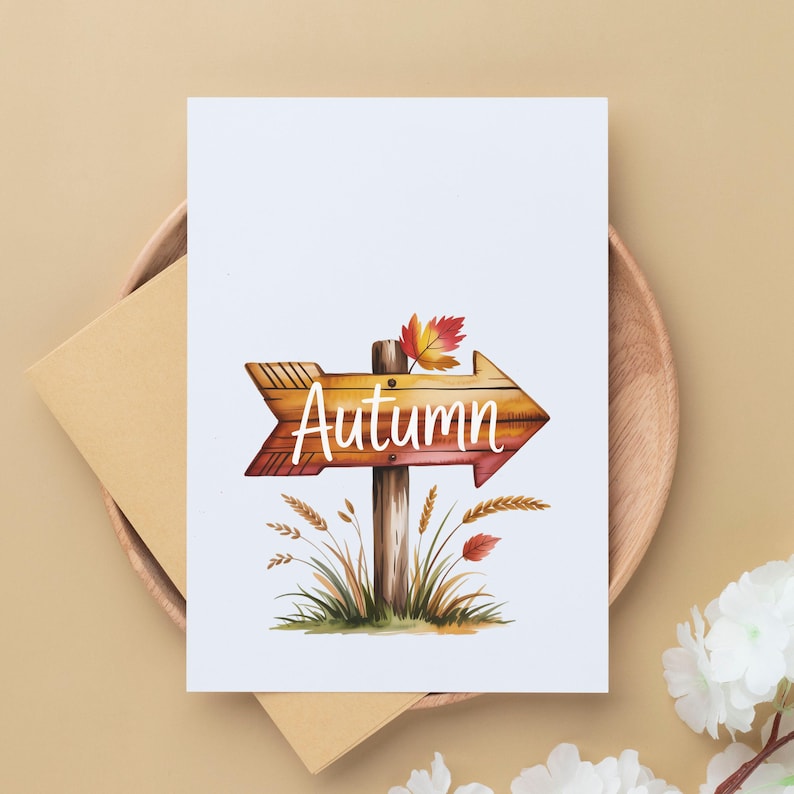 Pode incluir: Um cart&atilde;o branco com uma ilustra&ccedil;&atilde;o de uma placa de seta de madeira que diz "Autumn" em escrita branca. A placa &eacute; marrom com uma folha vermelha e amarela em cima. O cart&atilde;o est&aacute; em um prato de madeira com um envelope marrom.