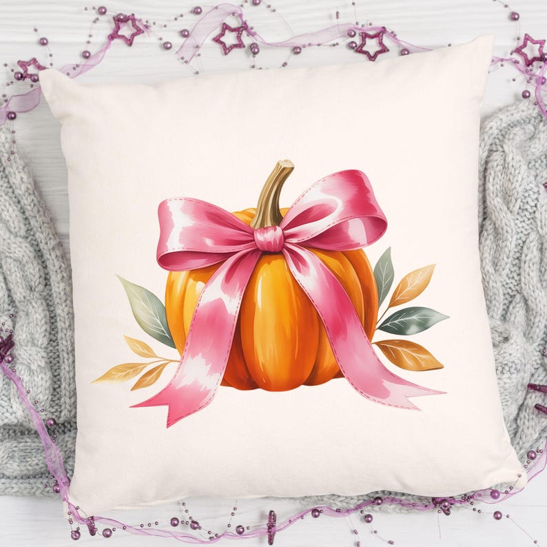 Pode incluir: Uma almofada quadrada decorativa com uma ilustra&ccedil;&atilde;o em aquarela de uma ab&oacute;bora laranja com um la&ccedil;o rosa. A ab&oacute;bora &eacute; adornada com folhas verdes e marrons. A almofada est&aacute; em um fundo branco.