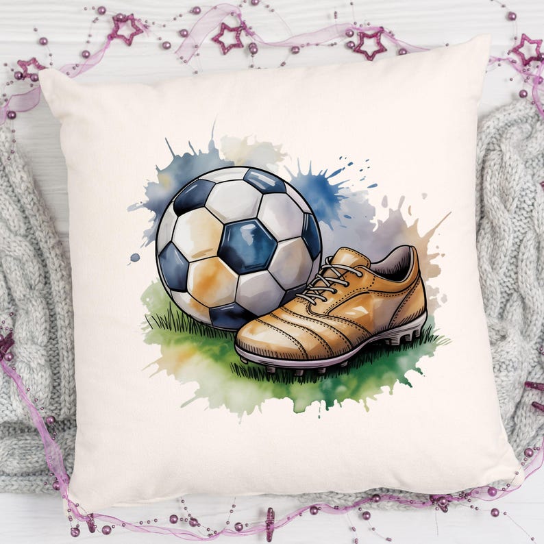 May include: A decorative pillow featuring a watercolor illustration of a soccer ball and a soccer cleat. The ball is white and black, and the cleat is tan. The background has blue and green watercolor splashes.