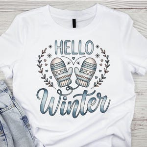 May include: White t-shirt featuring the words "HELLO Winter" in a blue gradient font, with a wreath of leaves and snowflakes. Two light blue mittens are in the center of the design.