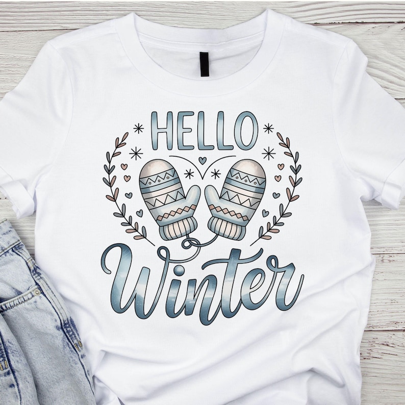 May include: White t-shirt featuring the words "HELLO Winter" in a blue gradient font, with a wreath of leaves and snowflakes. Two light blue mittens are in the center of the design.