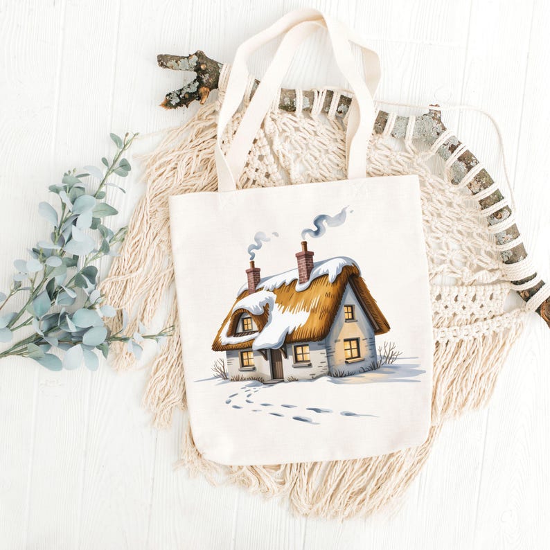 May include: A cream-colored tote bag featuring a watercolor illustration of a snow-covered cottage with a thatched roof. The cottage has two chimneys with smoke, and footprints lead to the door. The bag has two cream-colored handles.