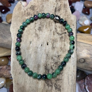 May include: A green and black gemstone bracelet with a silver clasp. The bracelet is made of small, round beads.