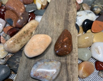 May include: Three smooth, polished stones on a weathered wooden surface. The stones are various shades of brown, white, and gray.