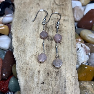 May include: A pair of silver dangle earrings with three pink gemstone beads on each earring.